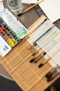 A detailed view of an artist's workspace featuring watercolor paints and brushes on a bamboo mat.